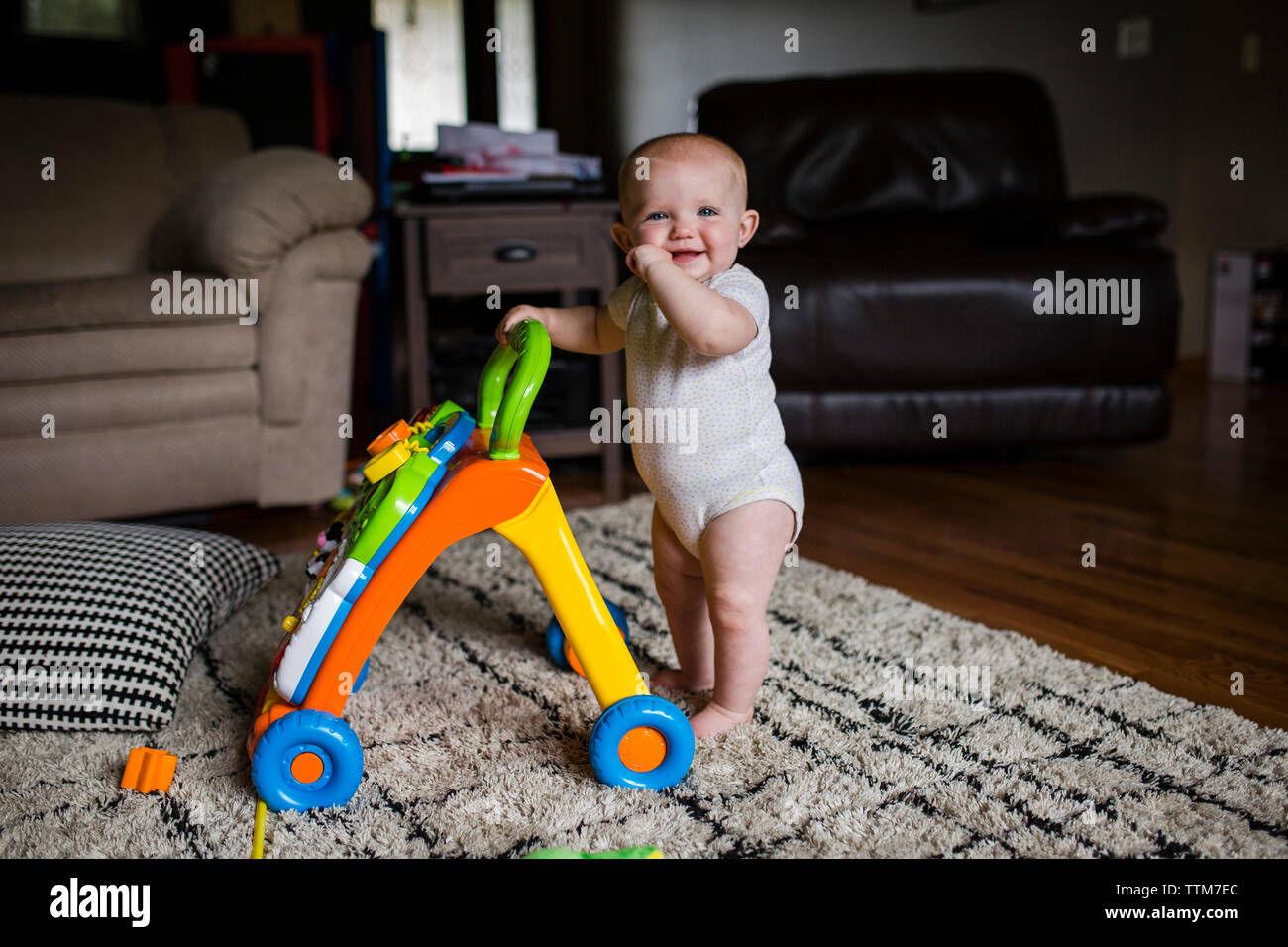 Portrait of happy baby girl with walker debout sur un tapis à la maison Banque D'Images