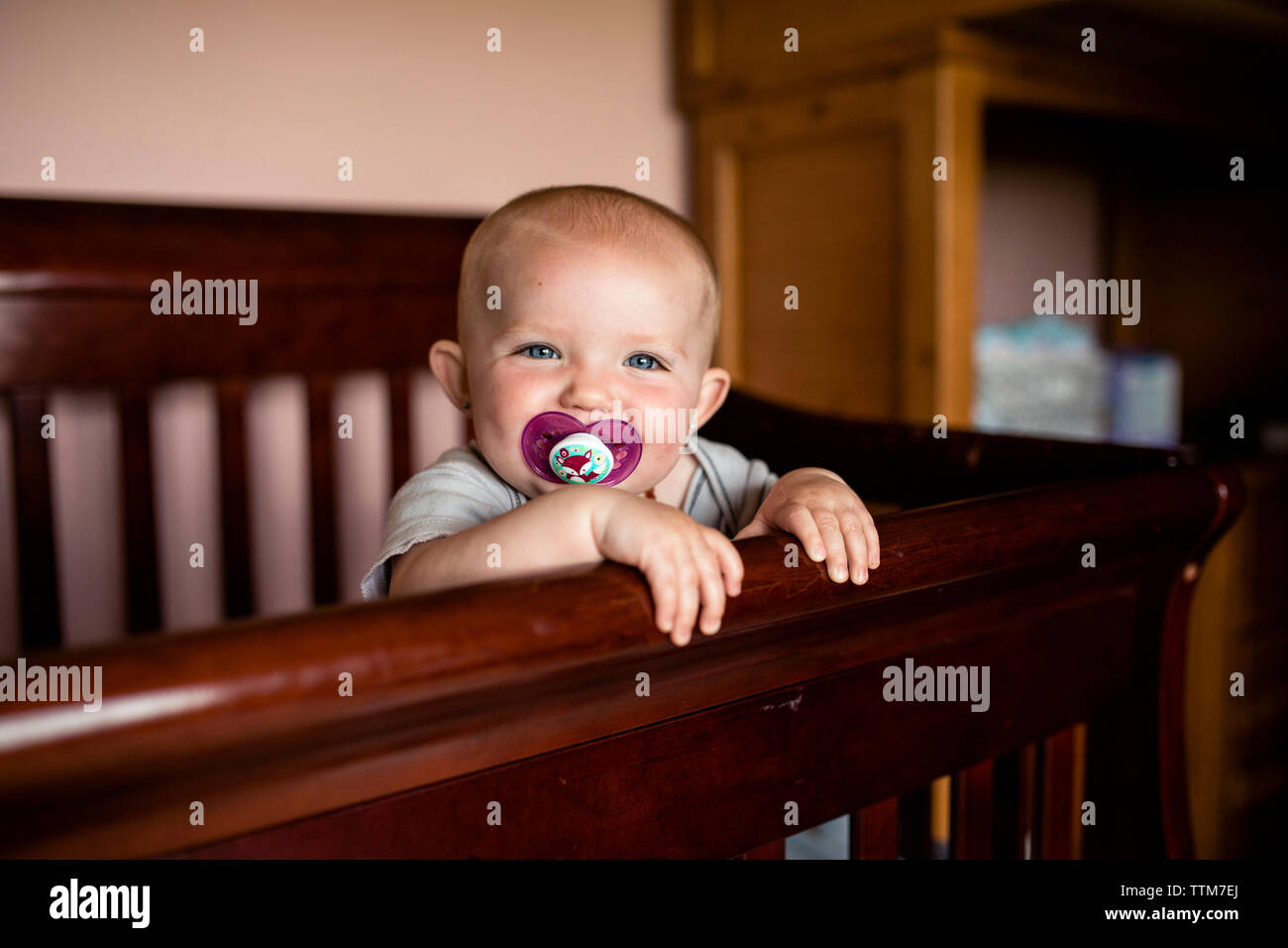 Portrait of happy baby girl sucking pacifier tout en se tenant dans un lit bébé Banque D'Images