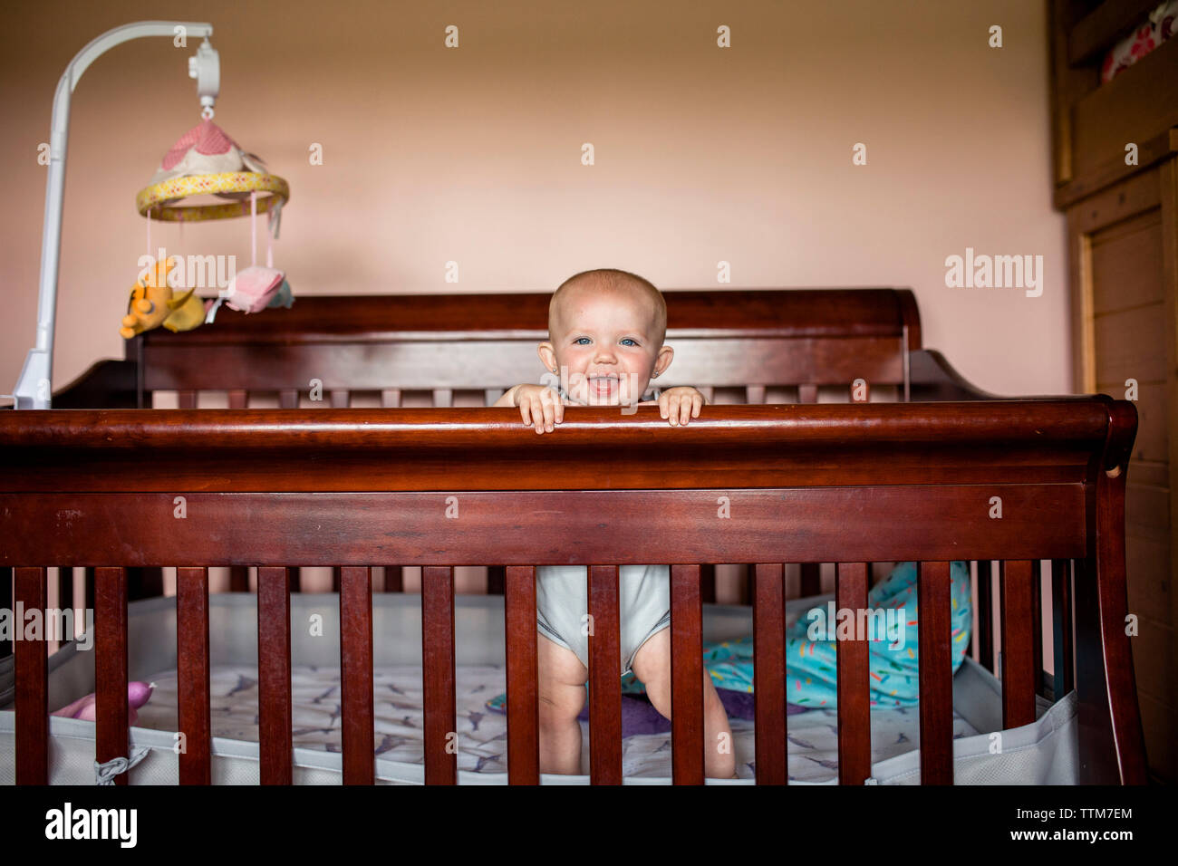 Portrait of happy baby girl standing in crib contre mur Banque D'Images