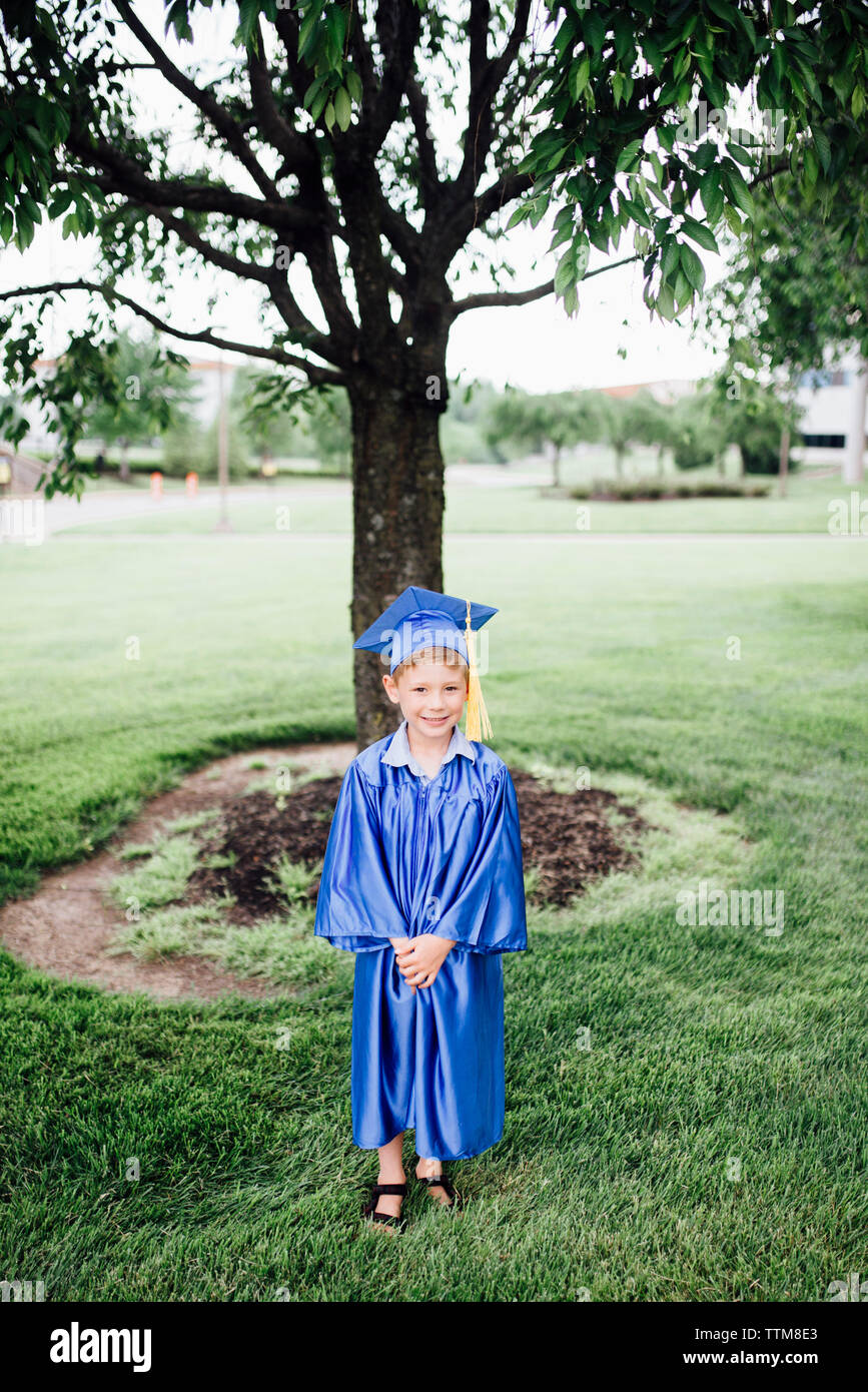 Portrait of boy in graduation gown standing on grassy field at park Banque D'Images