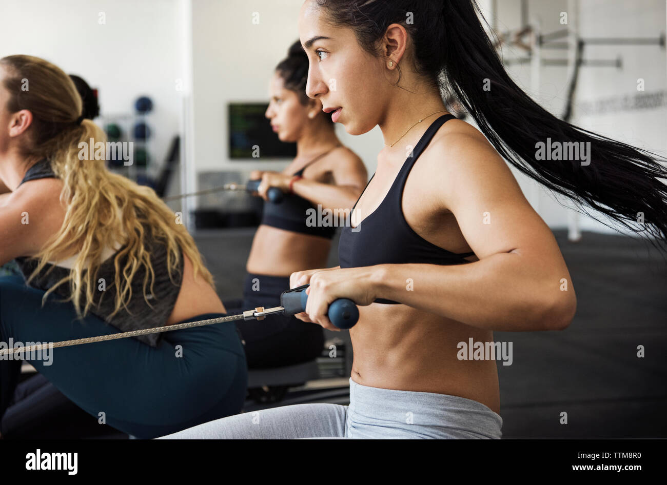 Les athlètes déterminés exerçant sur les machines à ramer en gym crossfit Banque D'Images