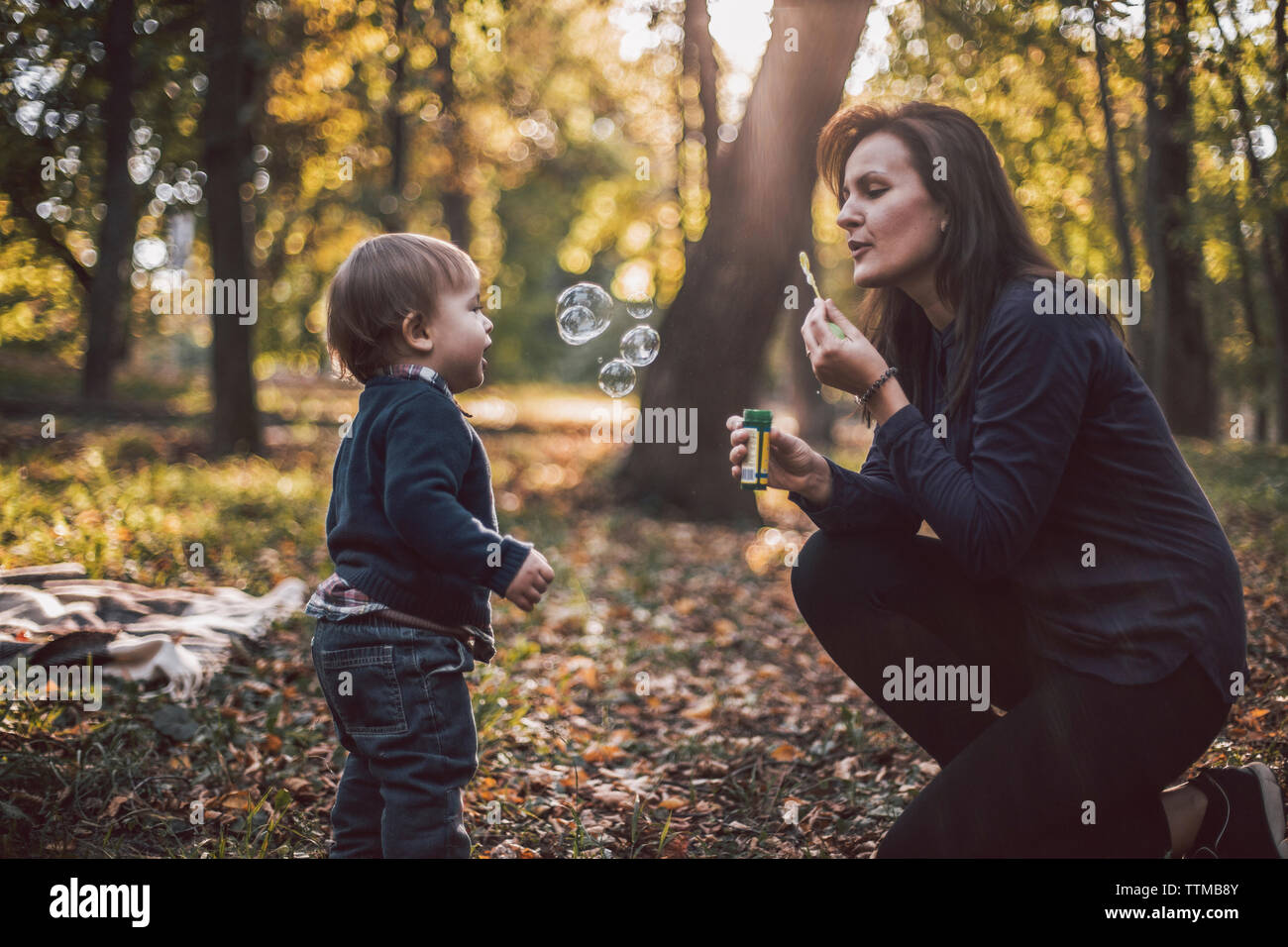 Mère et fils jouant avec bulles au parc en automne Banque D'Images