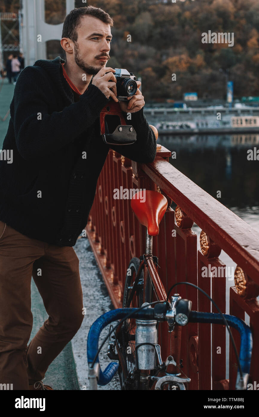 Photographier avec un appareil photo tout en cycliste avec permanent location sur pont en ville pendant le coucher du soleil Banque D'Images
