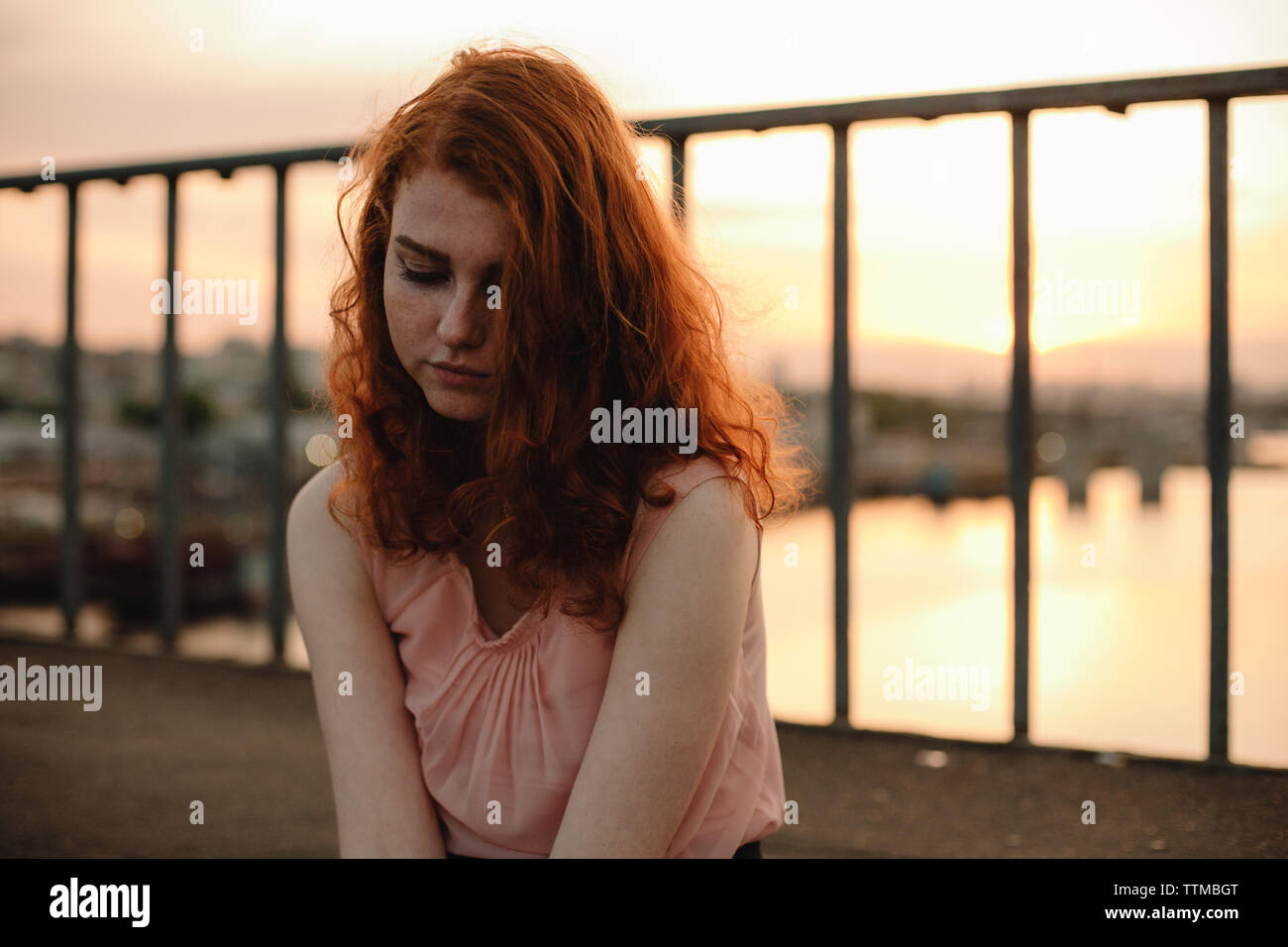 Portrait de jeune femme aux cheveux rouges assis sur le pont au coucher du soleil Banque D'Images
