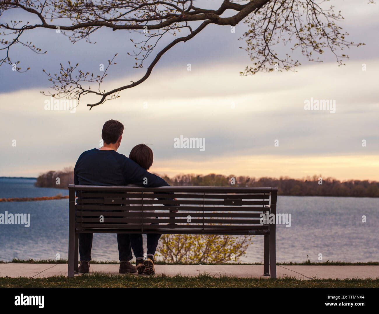 Père et fils à la vue de tout en restant assis sur banc de parc par le lac Banque D'Images