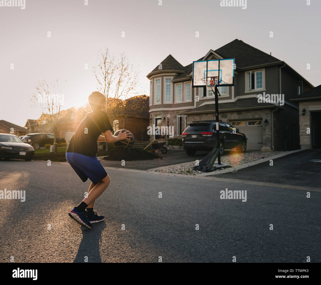 Toute la longueur du garçon jouant au basket-ball sur la route pendant le coucher du soleil Banque D'Images