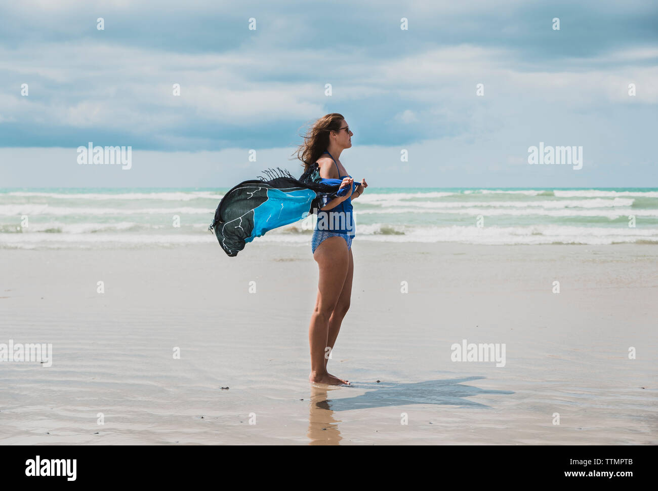 Side view of woman in swimwear holding sarong debout à la ciel nuageux au cours de journée ensoleillée Banque D'Images