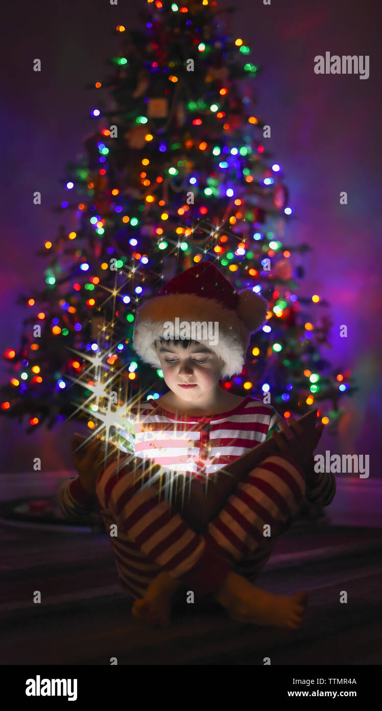 Jeune garçon lisant un livre magique en face de l'arbre de Noël. Banque D'Images