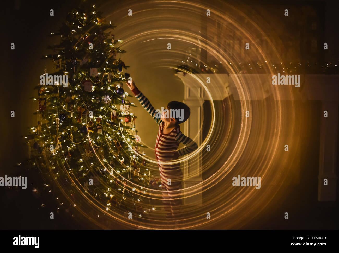 Boy decorating a Christmas Tree dans la nuit entouré d'anneaux lumineux. Banque D'Images
