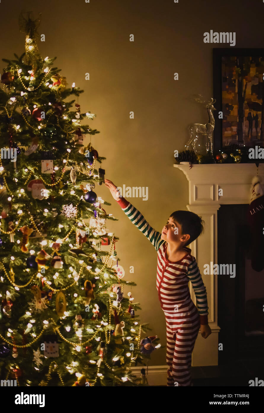 Jeune garçon décorer un arbre de Noël dans la nuit à côté d'une cheminée. Banque D'Images