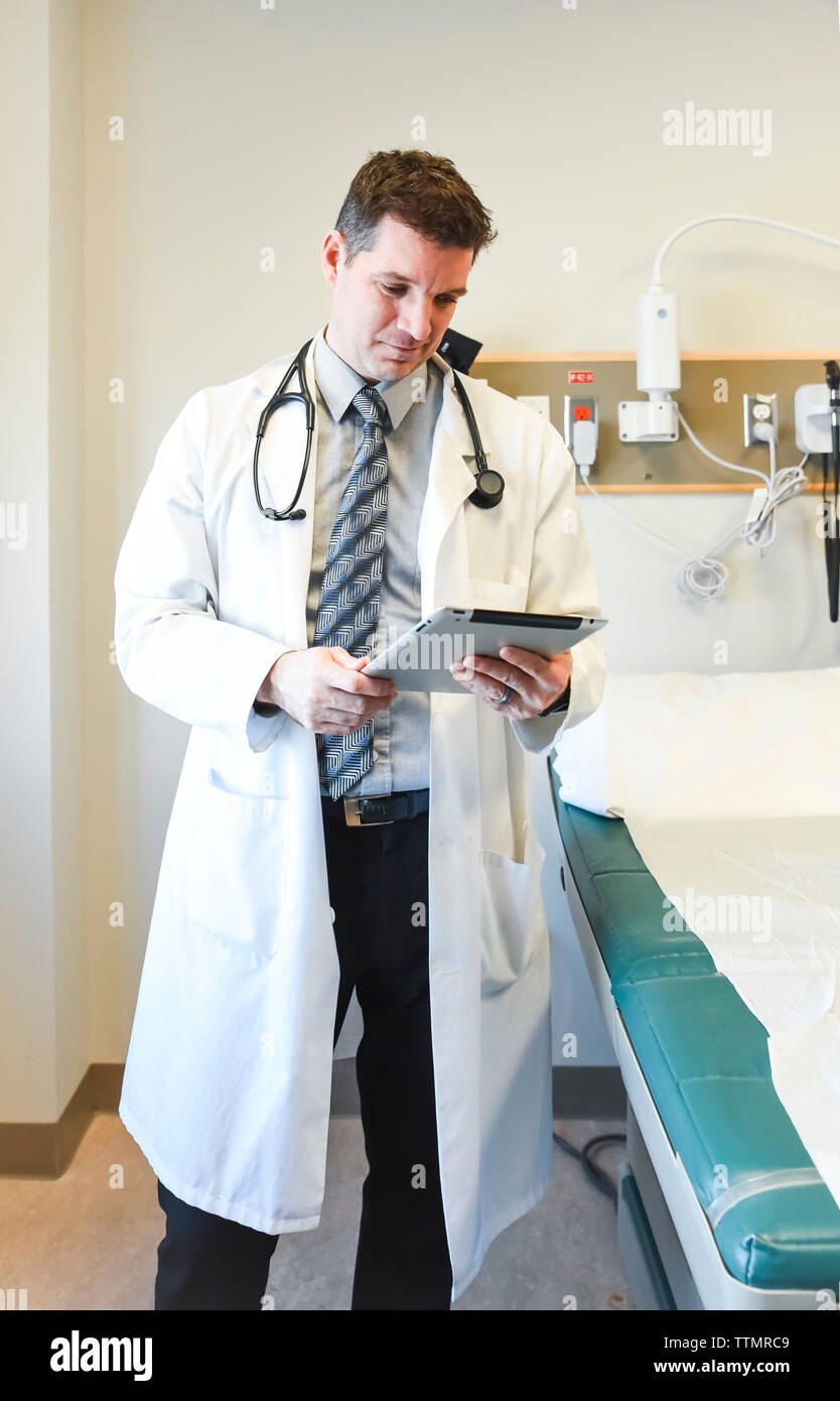 Un médecin en blouse blanche à côté de la table d'examen à l'hôpital à la recherche d'une tablette. Banque D'Images