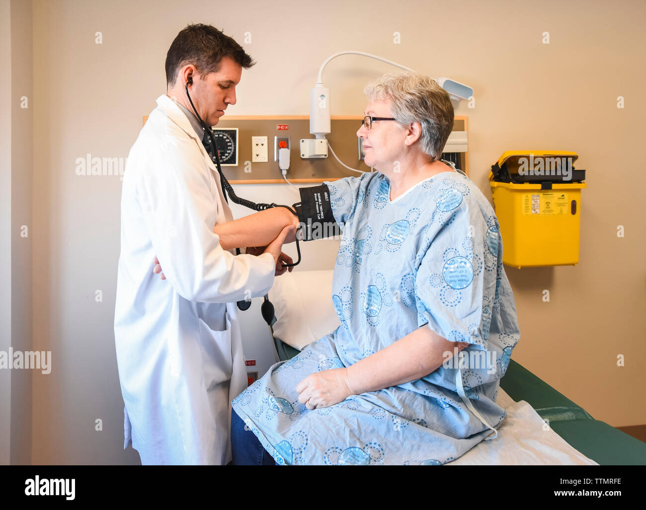 Médecin de prendre la tension artérielle du patient plus âgé en peignoir dans la salle de clinique. Banque D'Images