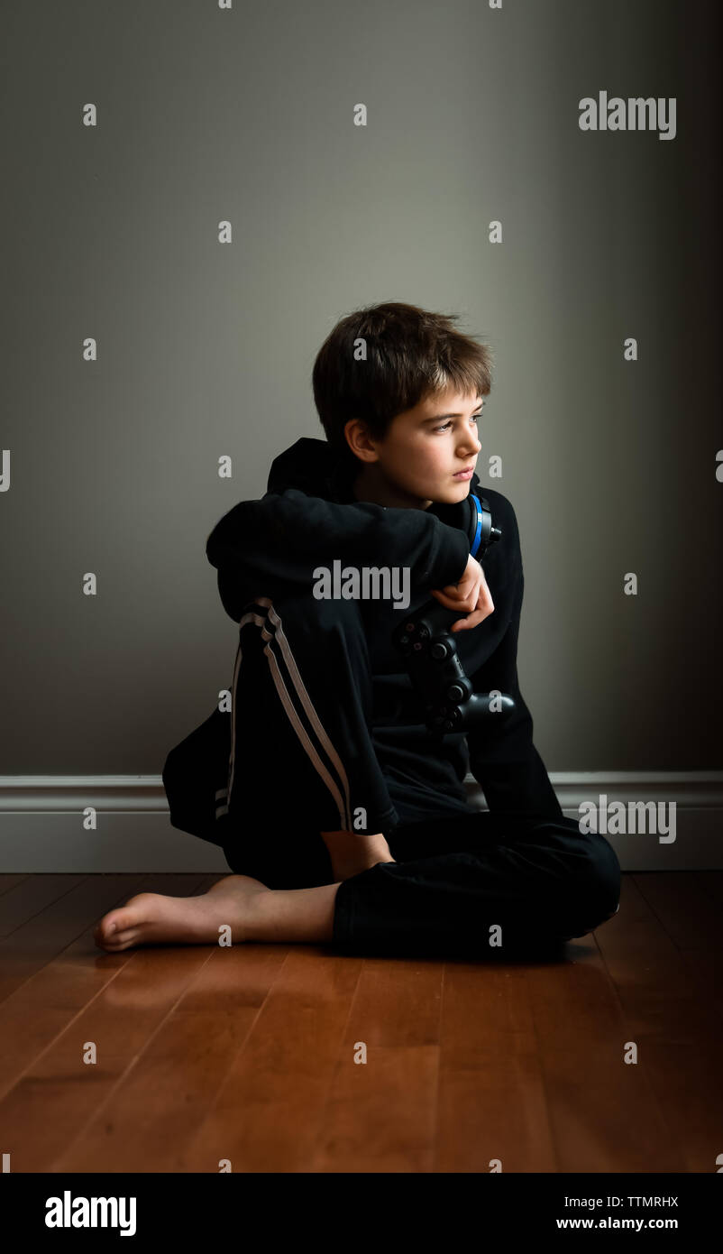 Preteen boy sitting on floor avec contrôleur de jeu vidéo dans la main. Banque D'Images