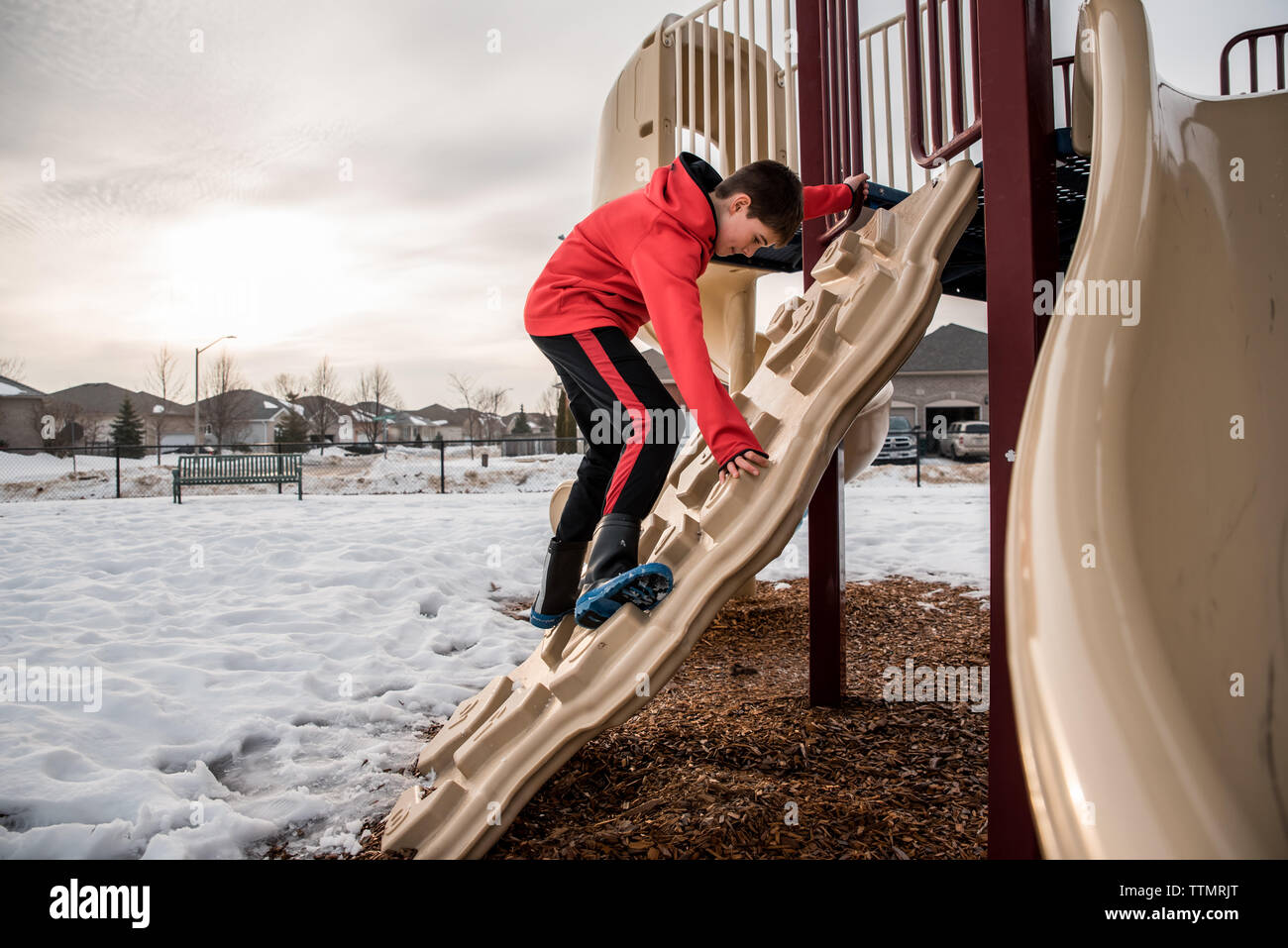 Garçon d'escalade sur structure de jeux dans un parc enneigé sur journée d'hiver. Banque D'Images