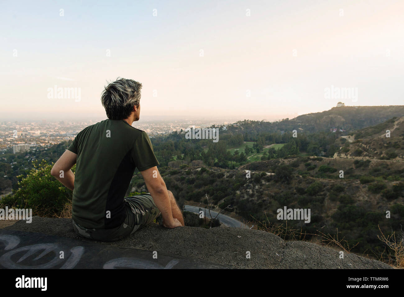 Young man looking at view while sitting on rock contre le ciel au coucher du soleil Banque D'Images