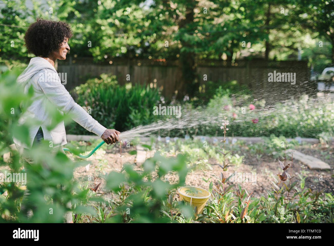 Vue de côté mature woman watering plants in garden Banque D'Images