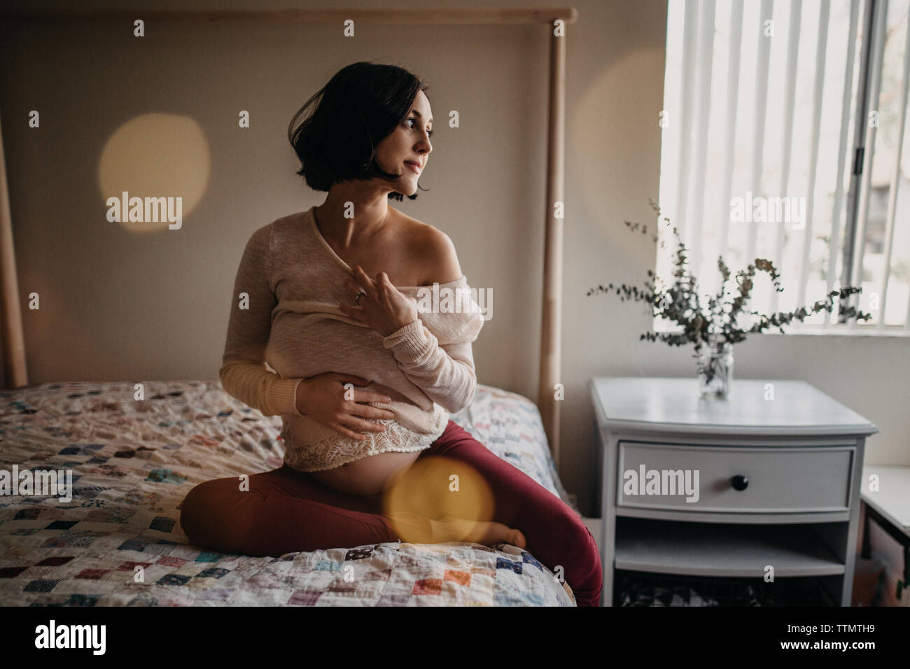 Pregnant woman holding baby bump au lit tout en souriant Banque D'Images