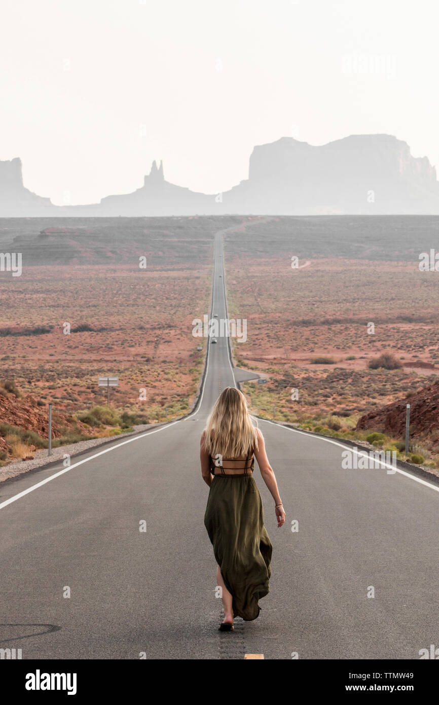 Vue arrière du female hiker marche sur route contre ciel clair à Monument Valley Tribal Park Banque D'Images