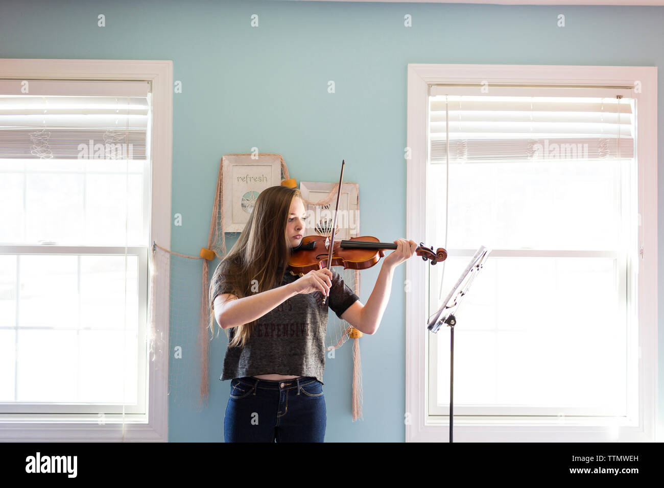 Femme à jouer du violon en position debout par fenêtre à la maison Banque D'Images