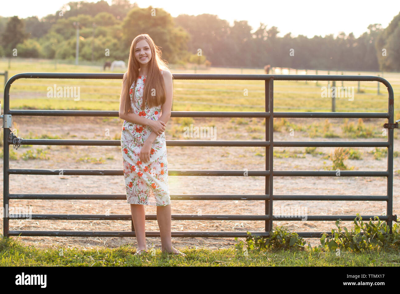 Smiling Teenage Girl standing in front of a Horse Farm Fence au coucher du soleil Banque D'Images