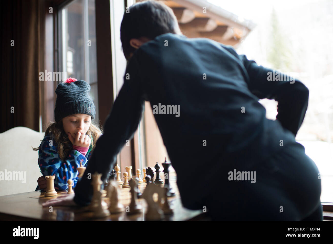 Frères et sœurs jouant aux échecs tout en se tenant à la fenêtre par Banque D'Images