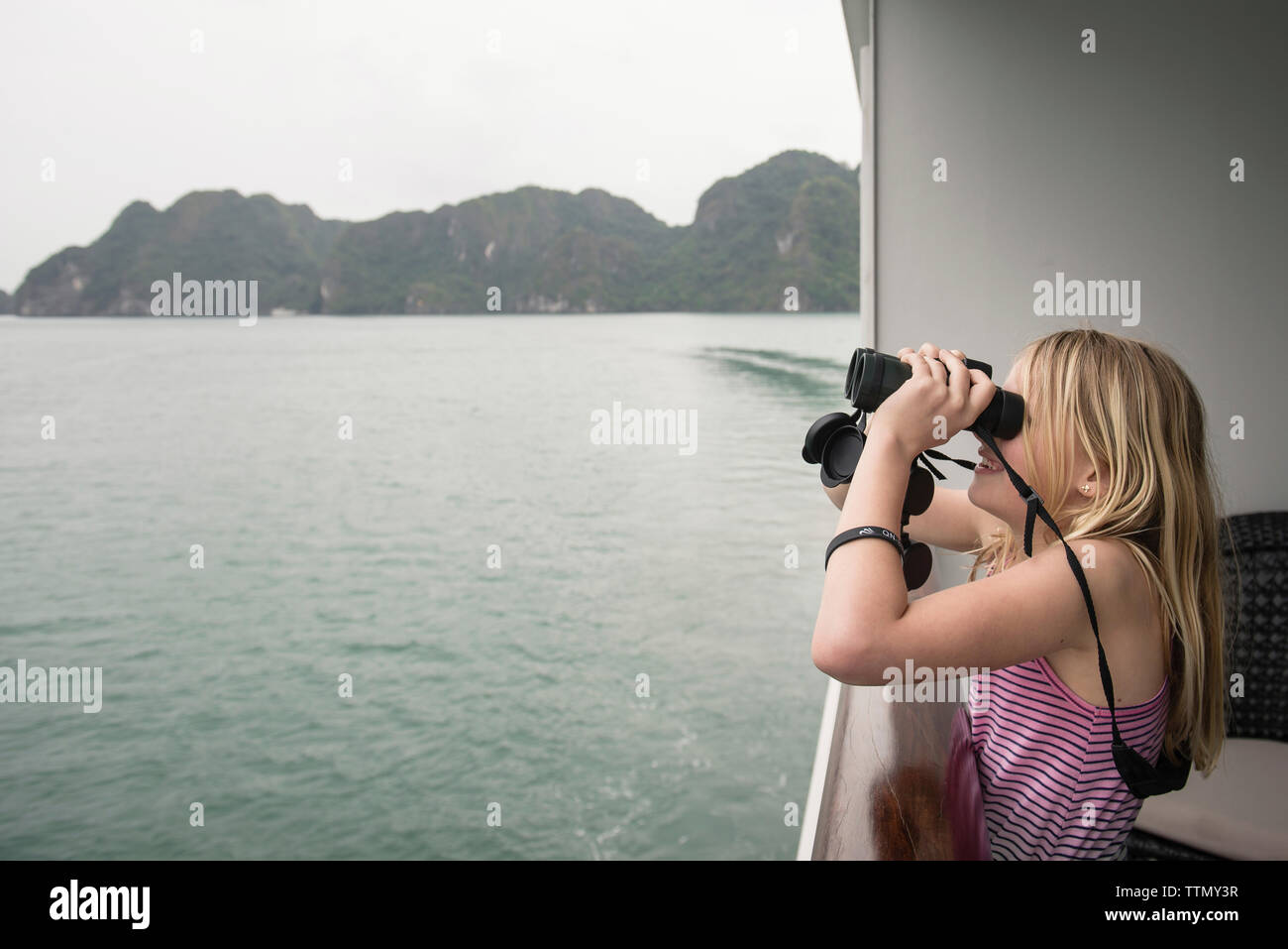 Vue latérale du girl looking through binoculars debout en bateau sur mer contre sky Banque D'Images