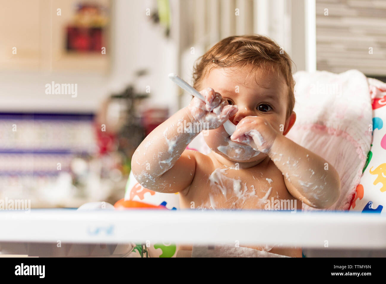Bébé colorées avec du yaourt en mangeant des yaourts dans sa chaise haute pour manger Banque D'Images