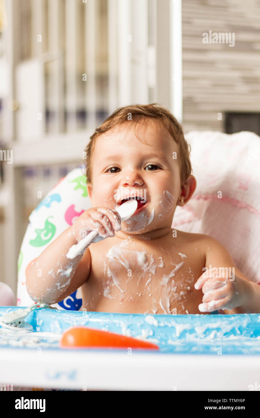 Bébé colorées avec du yaourt en mangeant des yaourts dans sa chaise haute pour manger Banque D'Images