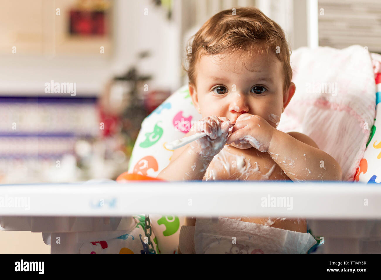 Bébé colorées avec du yaourt en mangeant des yaourts dans sa chaise haute pour manger Banque D'Images