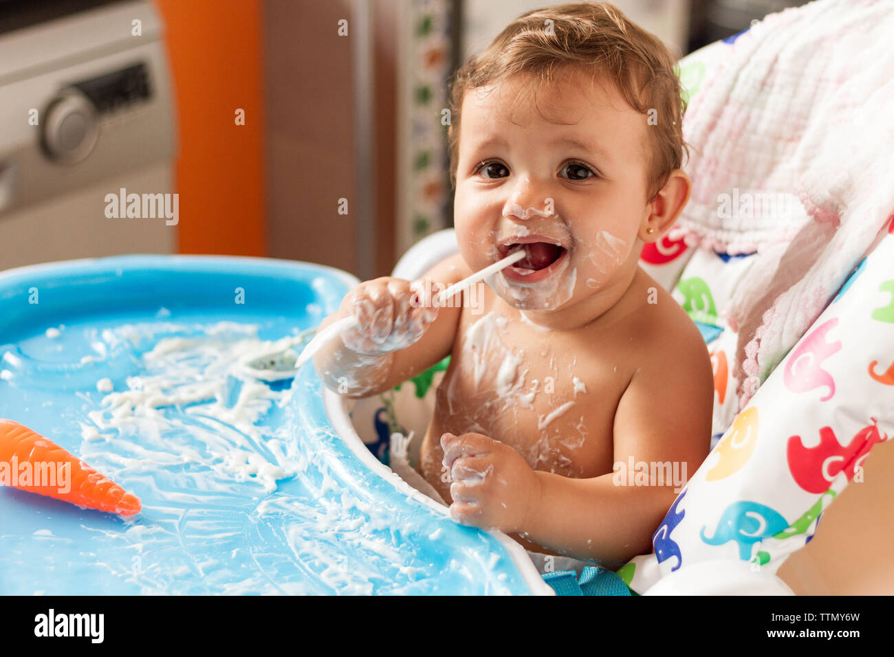 Bébé colorées avec du yaourt en mangeant des yaourts dans sa chaise haute pour manger Banque D'Images
