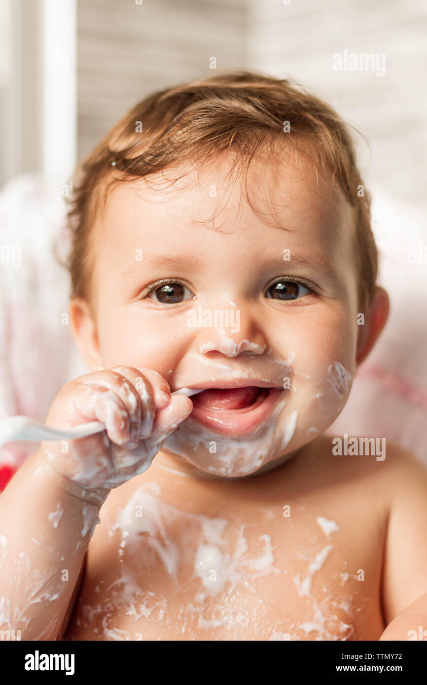Bébé colorées avec du yaourt en mangeant des yaourts dans sa chaise haute pour manger Banque D'Images