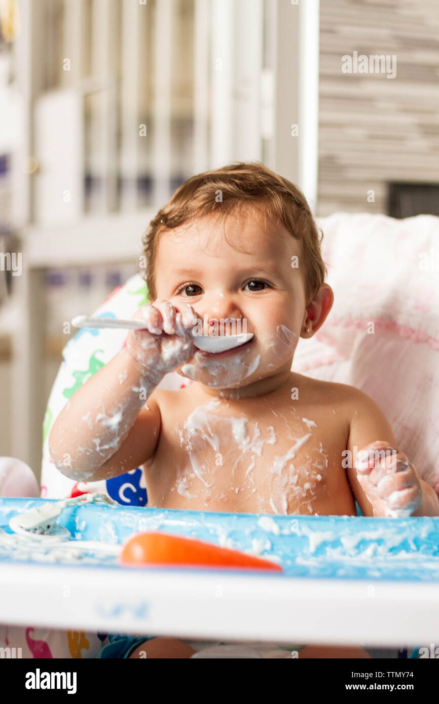 Bébé colorées avec du yaourt en mangeant des yaourts dans sa chaise haute pour manger Banque D'Images