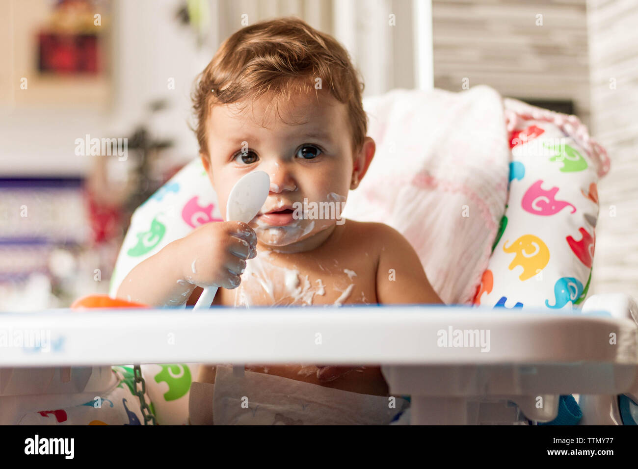Bébé colorées avec du yaourt en mangeant des yaourts dans sa chaise haute pour manger Banque D'Images