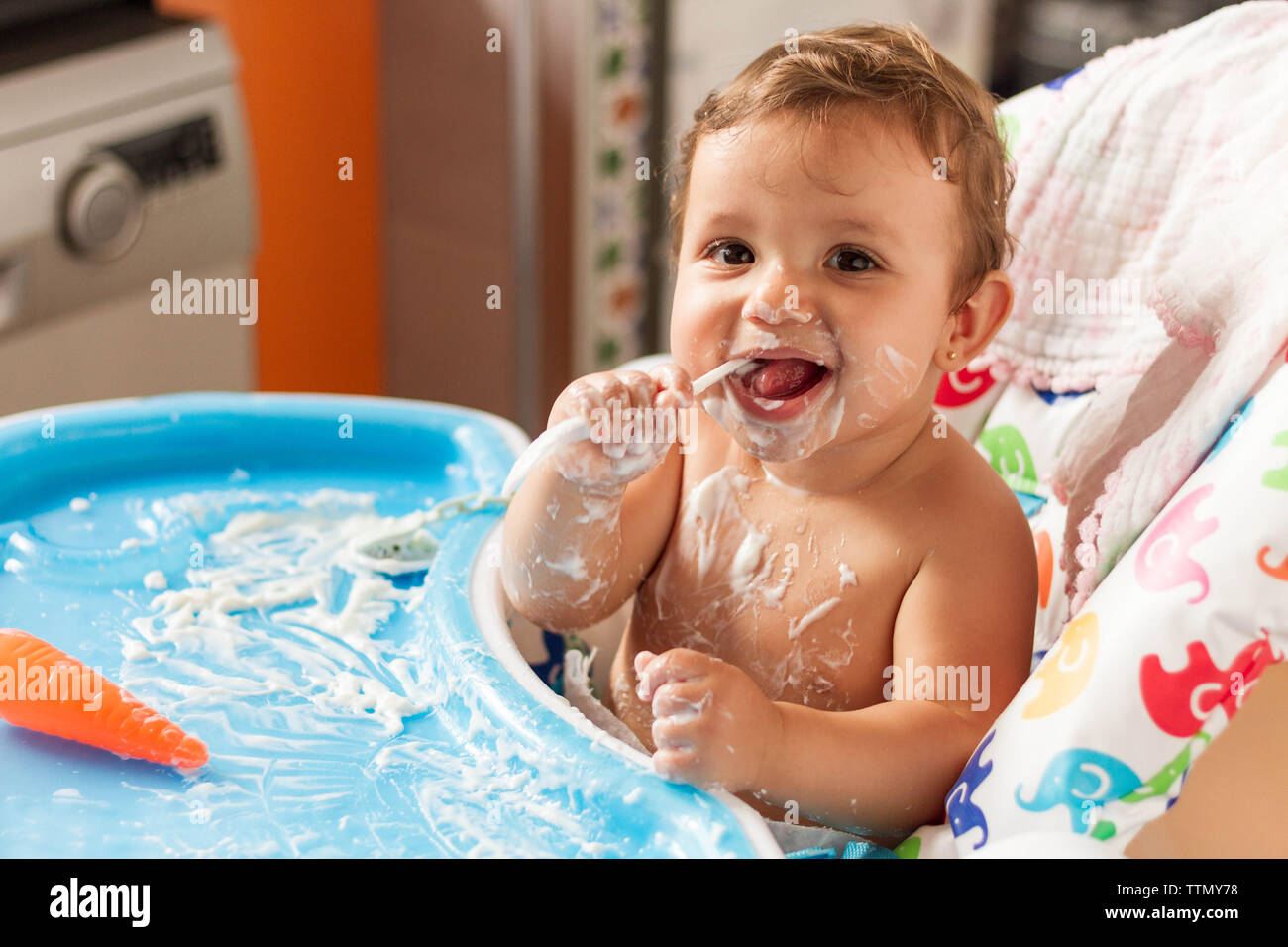 Bébé colorées avec du yaourt en mangeant des yaourts dans sa chaise haute pour manger Banque D'Images