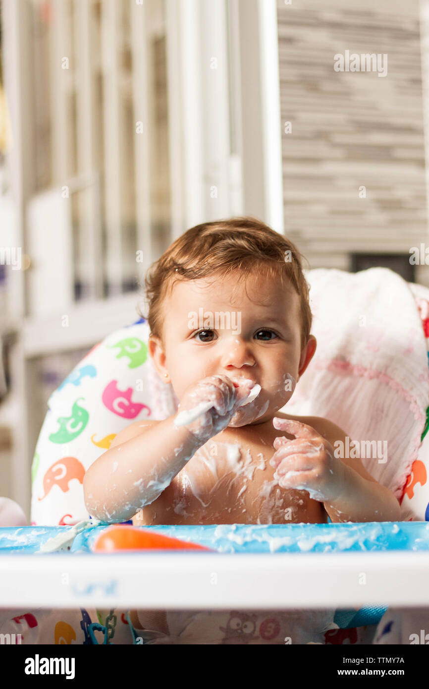 Bébé colorées avec du yaourt en mangeant des yaourts dans sa chaise haute pour manger Banque D'Images