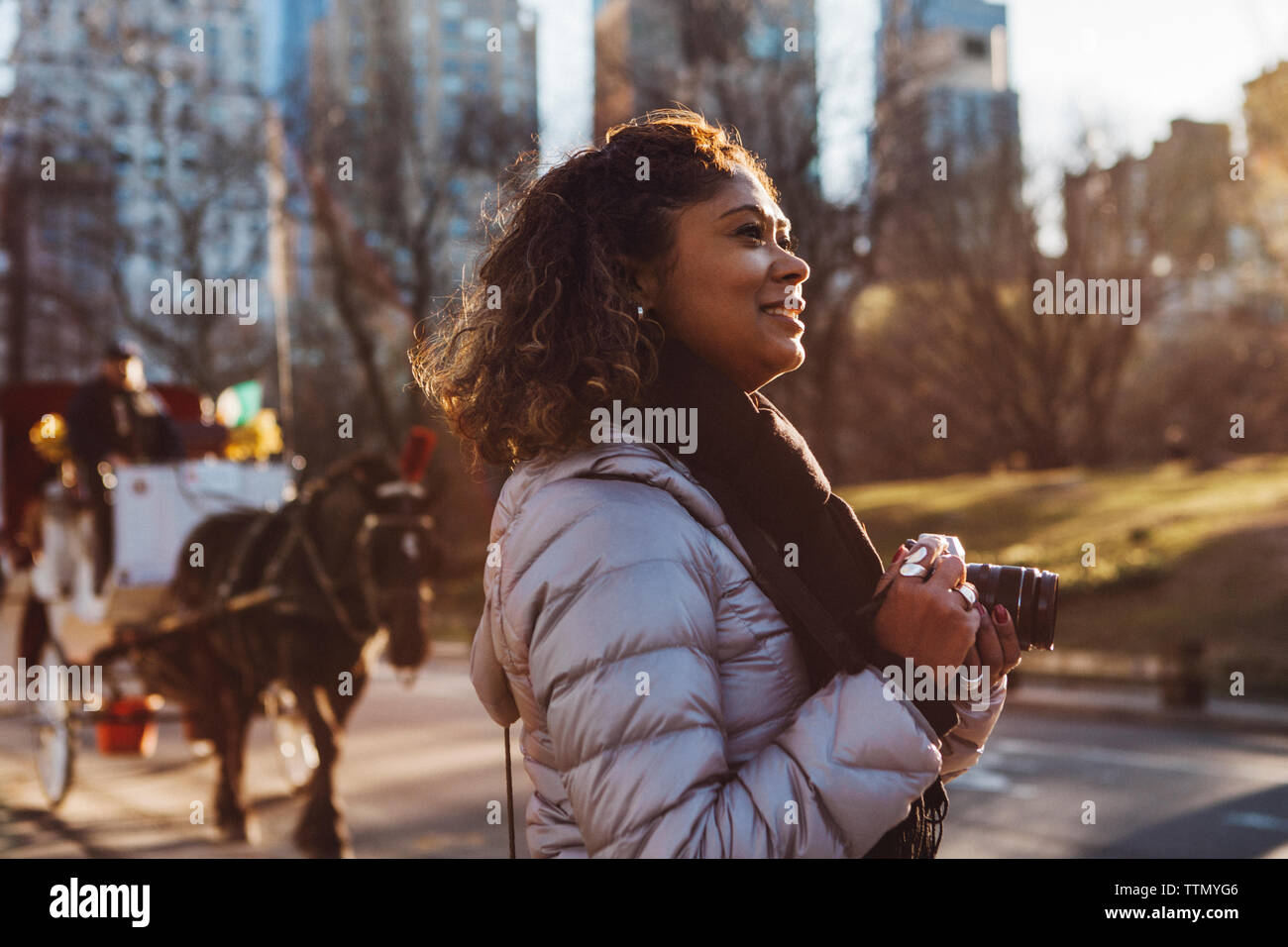 Vue latérale du smiling woman holding digital camera on city street Banque D'Images