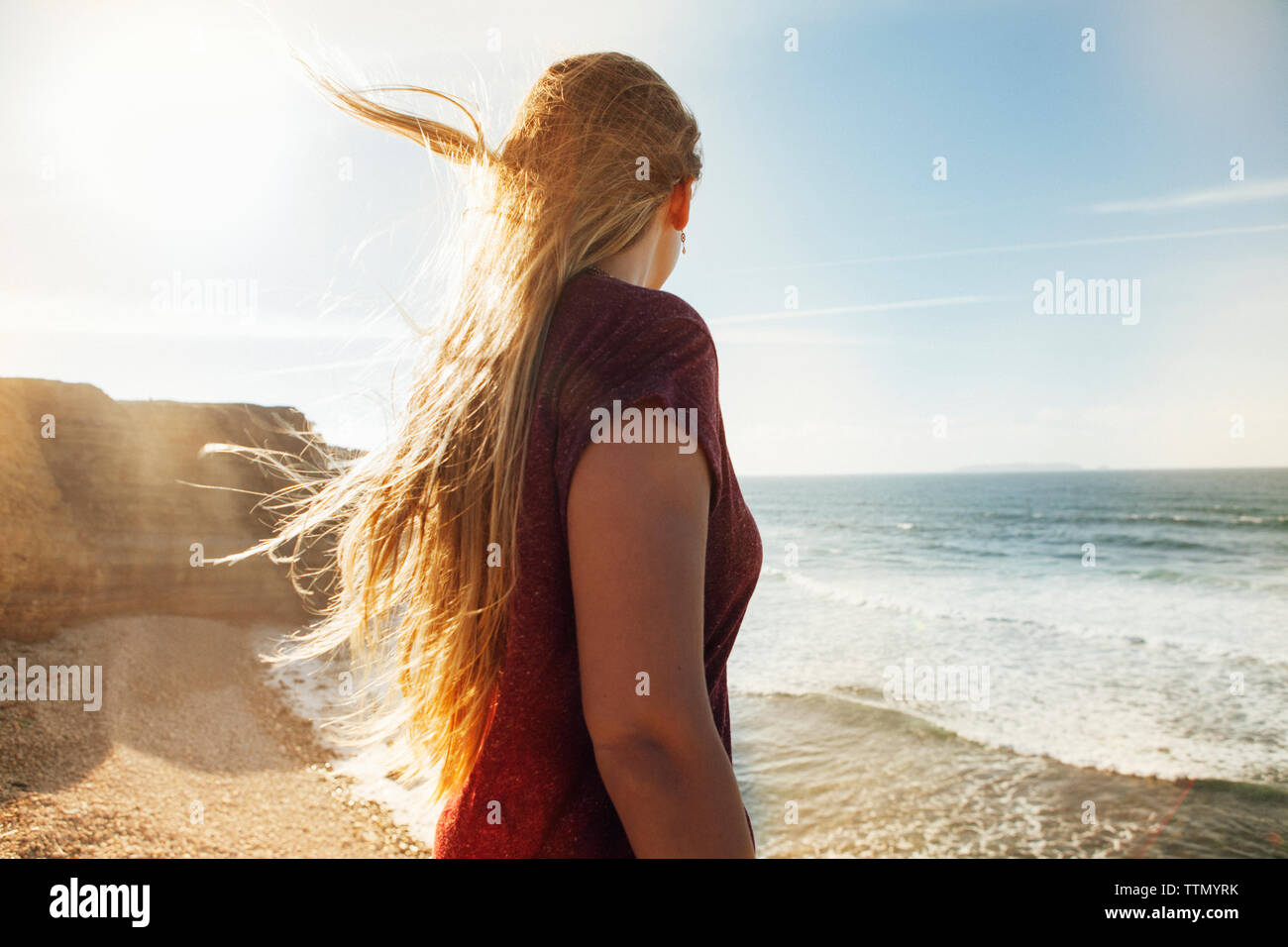 Vue latérale du woman looking at view tout en se tenant à jour ensoleillé sur la plage Banque D'Images