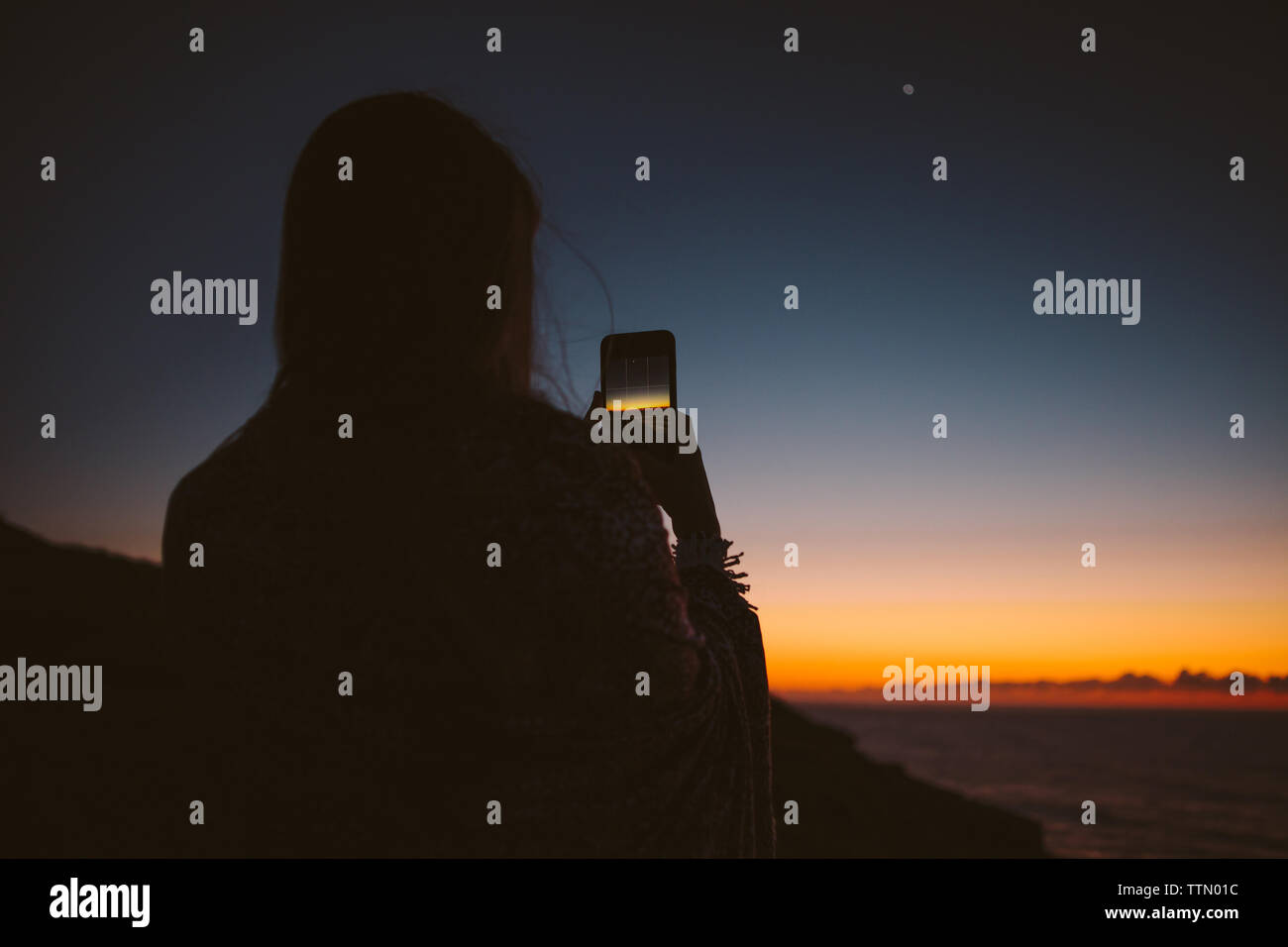 Rear view of woman photographing coucher du soleil par le biais de smart phone Banque D'Images