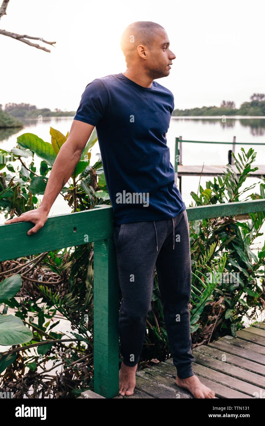 Toute la longueur du jeune homme à la vue à en se tenant sur le pier contre des plantes et le lac Banque D'Images