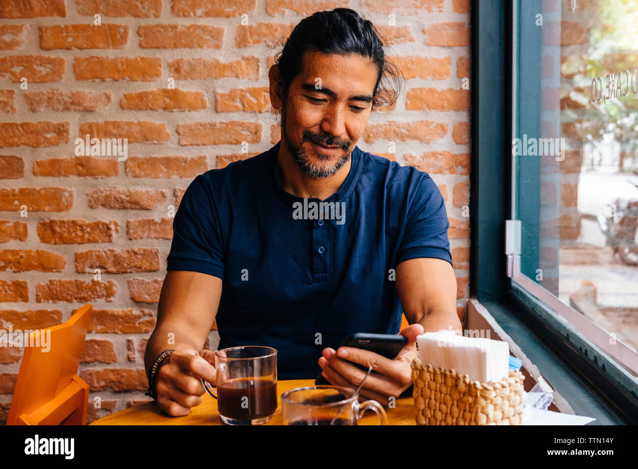 Homme mature avec du café noir à l'aide de smart phone against brick wall in cafe Banque D'Images Homme mature avec du café noir à l'aide de smart phone against brick wall in cafe Banque D'Images