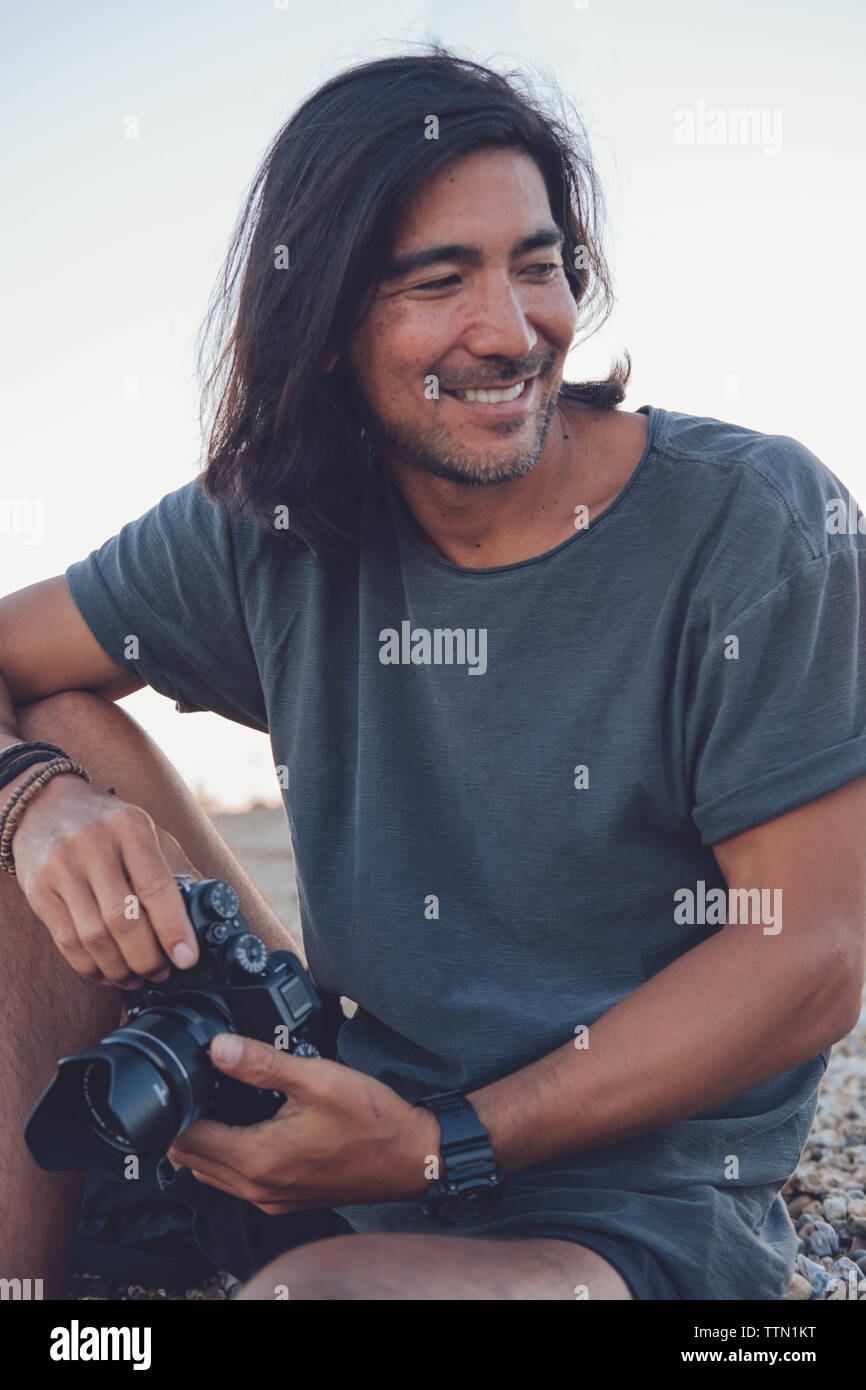 Personne souriante à l'appareil photo sur la plage tout en tenant son appareil photo Banque D'Images