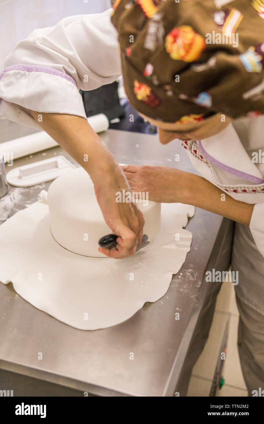 High angle view of female baker pâte à gâteau de coupe avec le coupe-pizza sur compteur de cuisine in laboratory Banque D'Images