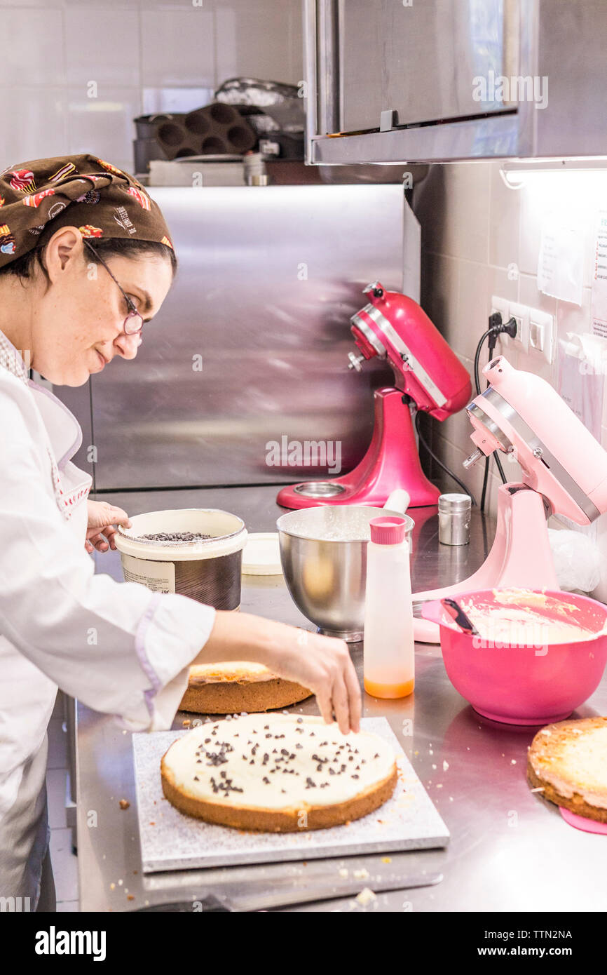 Vue de côté femme baker decorating cake aux pépites de chocolat sur le comptoir de la cuisine au laboratoire Banque D'Images