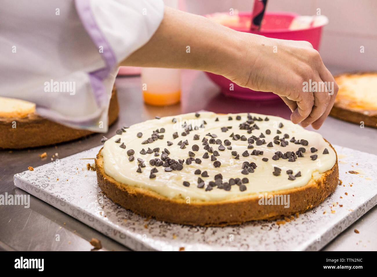 Main de femme cultivée baker decorating cake aux pépites de chocolat sur le comptoir de la cuisine au laboratoire Banque D'Images