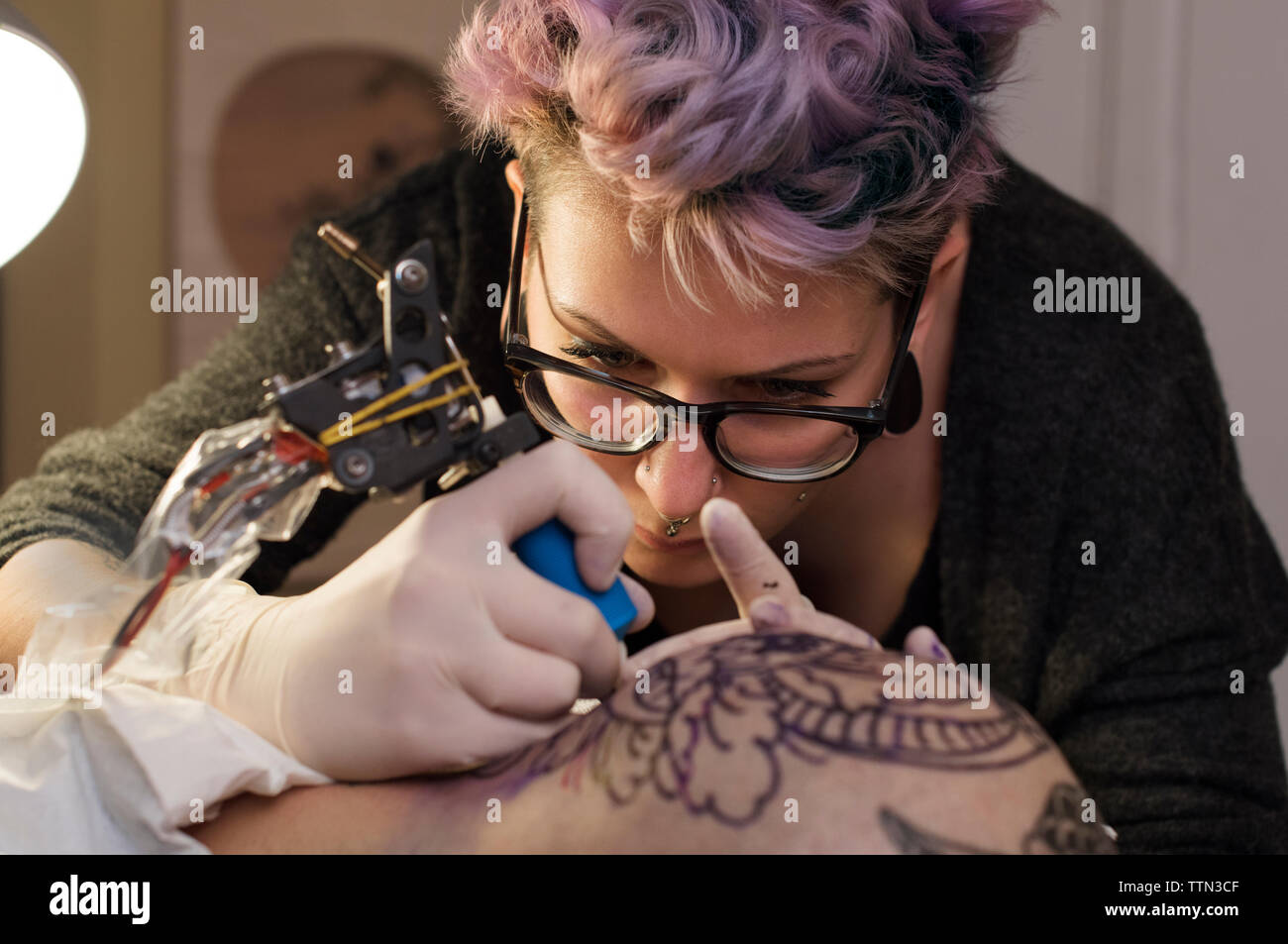 Femme artiste de tatouage tatouage tête de client en studio Banque D'Images
