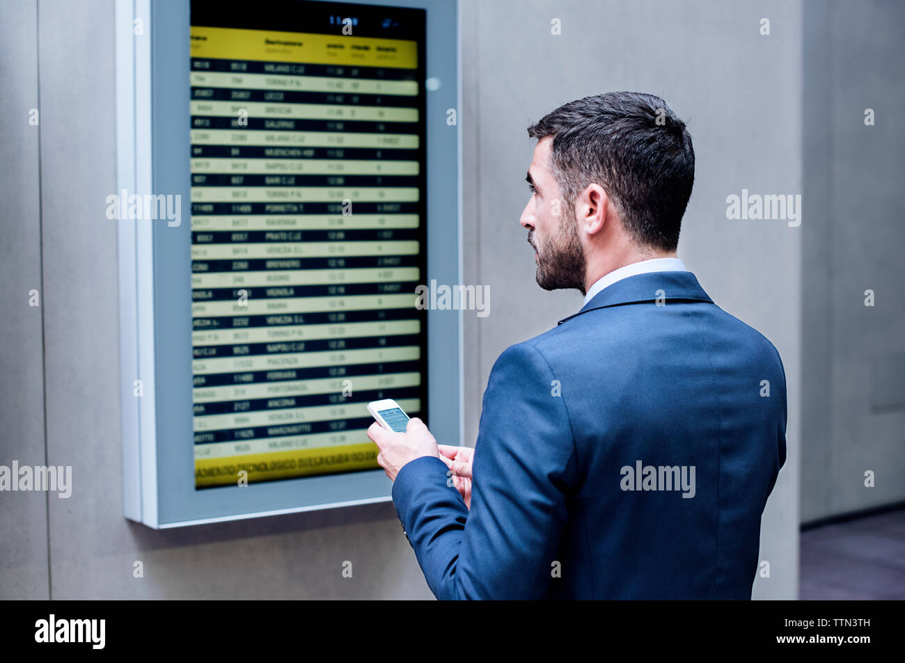 Vue arrière du businessman holding smart phone pendant la lecture arrivée départ à subway station Banque D'Images