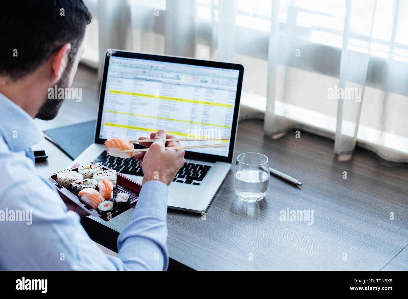 Vue latérale du businessman eating sushi lors de l'utilisation de l'ordinateur portable sur appui de fenêtre dans la chambre d'hôtel Banque D'Images