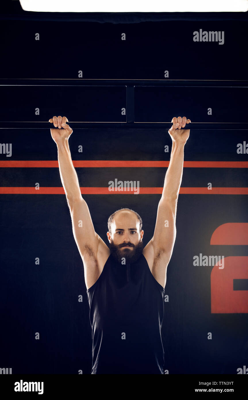 Portrait of male athlete hanging from monkey bar in gym Banque D'Images