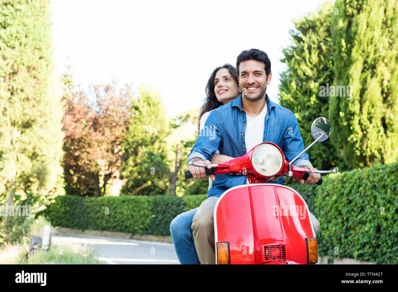 Smiling couple riding on motor scooter à park Banque D'Images