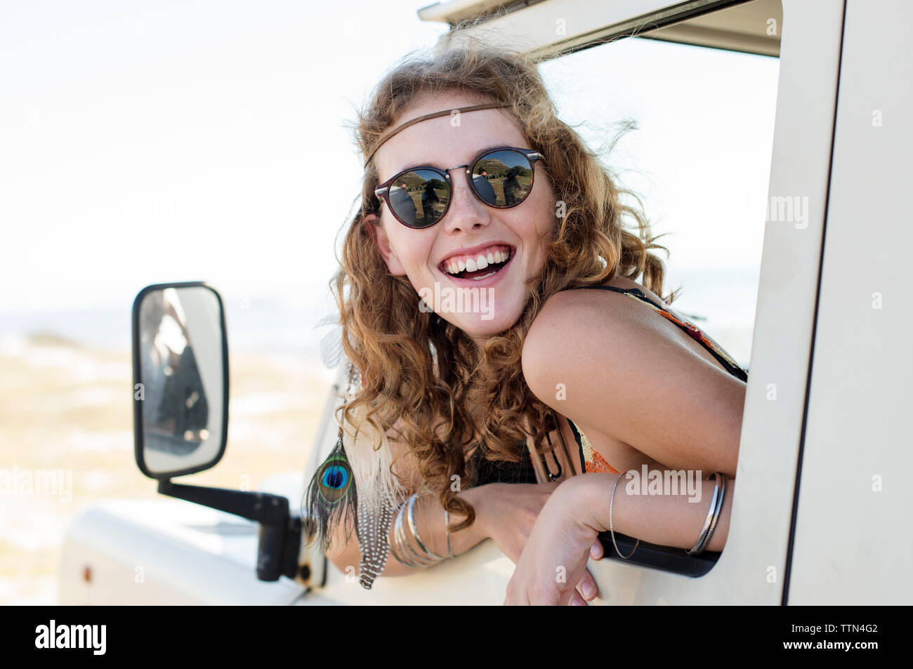 Happy woman wearing sunglasses peeking through car window Banque D'Images